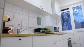 A kitchen with white cabinets, a microwave, and a window with a view of trees. - Joy City Stay Versului 8 (Timișoara)