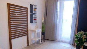 A modern room with a wooden slat partition, a white console table, a small black shelf with decorative items, a potted plant, and a view through a large window with curtains. - Joy City Stay Versului 8 (Timișoara)