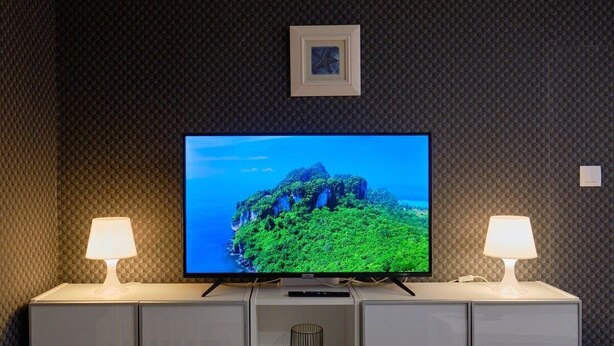 A flat-screen TV on a cabinet with two lamps, a picture frame, and a shelf with a decorative item. - Joy City Stay Versului 8 (Timișoara)