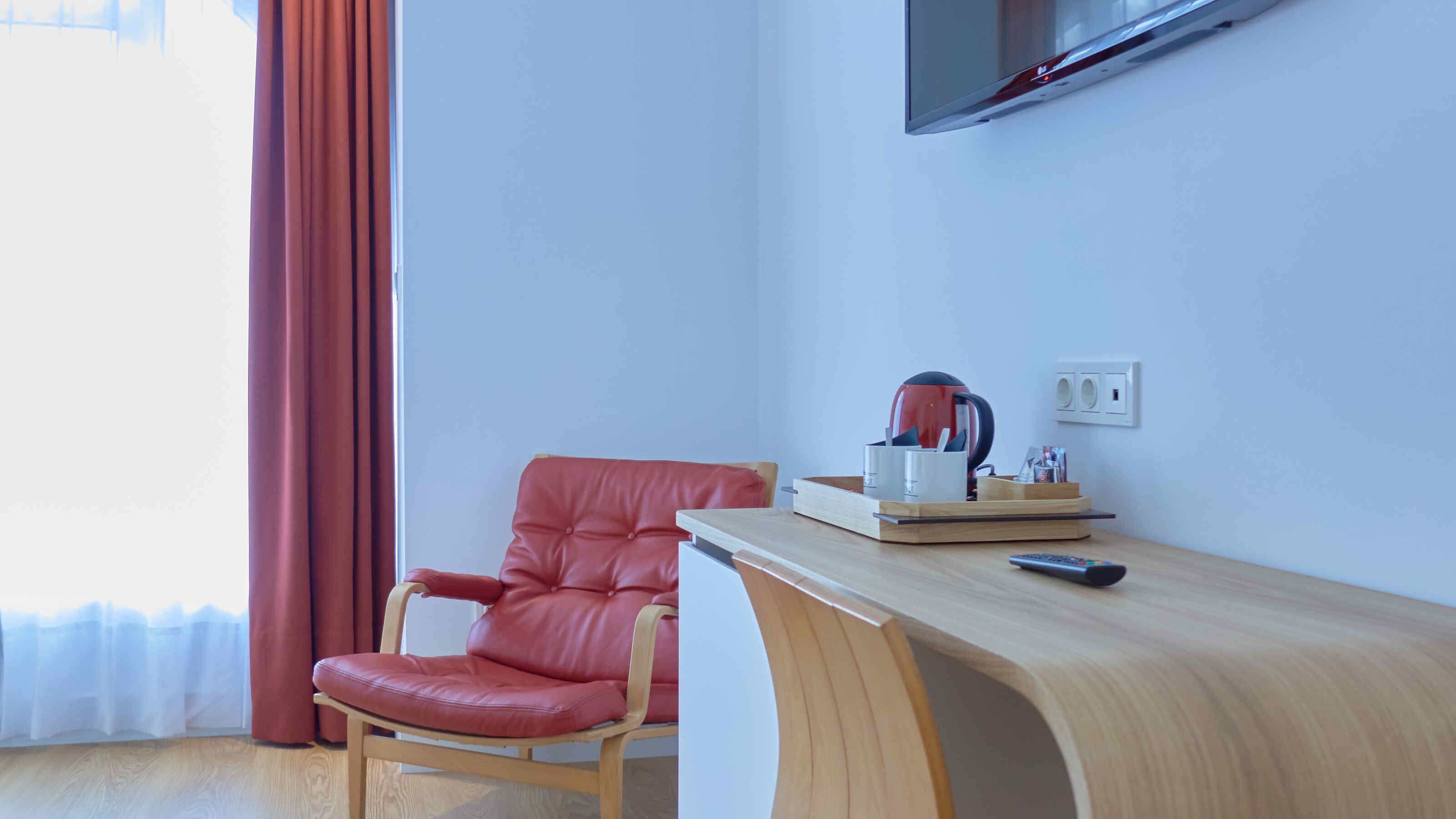 Una habitación moderna con un sillón de cuero, un escritorio de madera, un televisor montado y una cafetera.