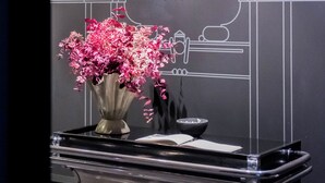 A reception desk with a black background and white architectural line drawings. A vase with pink flowers is placed on the desk. - BoulevArt Donostia (San Sebastián)