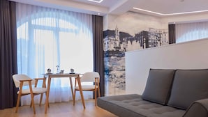 A modern living room with a grey sofa, wooden chairs, a small table with two bowls and a vase, and a large window with sheer curtains. - BoulevArt Donostia (San Sebastián)