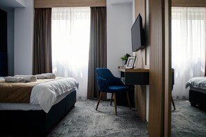 A hotel room with two beds, a desk with a chair, a television, and a view of the outdoors through large windows. - GBU Home - Azure Room (Timișoara)