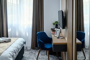 A hotel room with a bed, a desk with a chair, a TV, and a plant. - GBU Home - Azure Room (Timișoara)