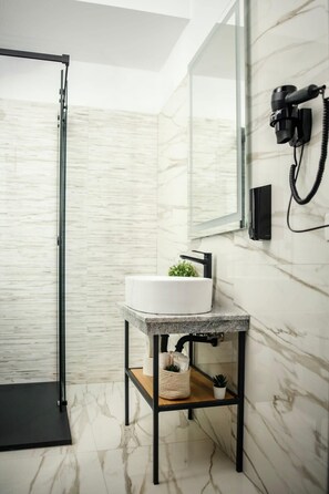 A modern bathroom with a glass shower enclosure, a white sink with a marble countertop, and a black hairdryer mounted on the wall. - GBU Home - Azure Room (Timișoara)