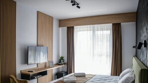 A modern hotel room with a bed, a desk, a television, and a window with curtains. - GBU Home - Olive Room (Timișoara)