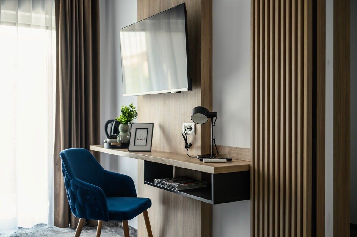 A modern room with a mounted TV, a desk with a lamp, and a blue chair.