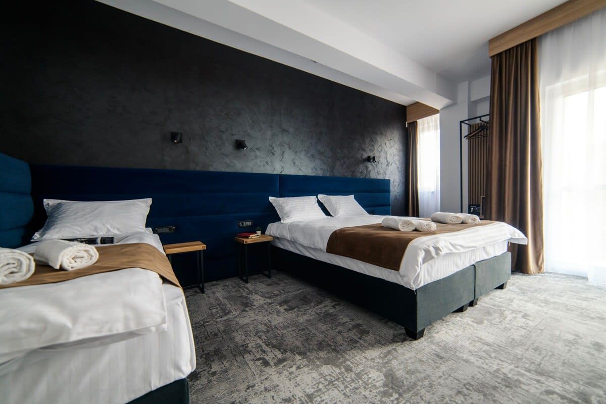A hotel room with two beds, a dark wall, a wooden headboard, and a large window with curtains.