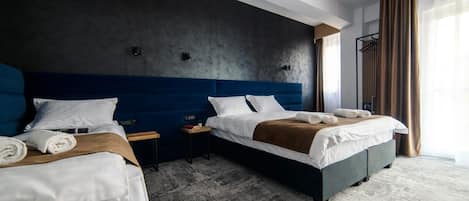 A hotel room with two beds, a dark wall, a wooden headboard, and a large window with curtains.