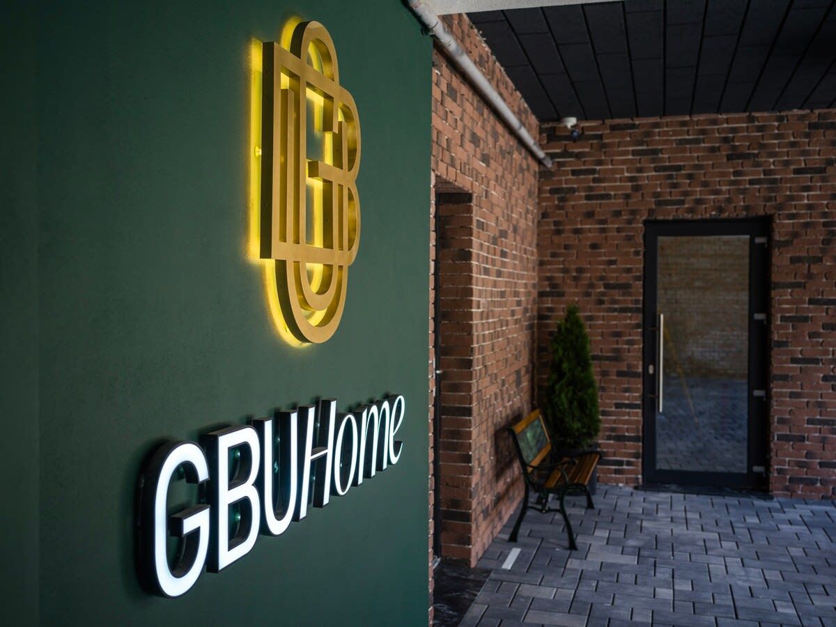 Ingresso di un edificio con un cartello che riporta 'GBUHome' e un muro in mattoni.