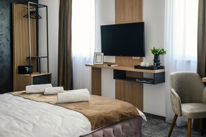 A hotel room with a bed, a TV mounted on a wooden panel, a chair, and a plant on a side table. - GBU Home - Pink Room 204 (Timișoara)