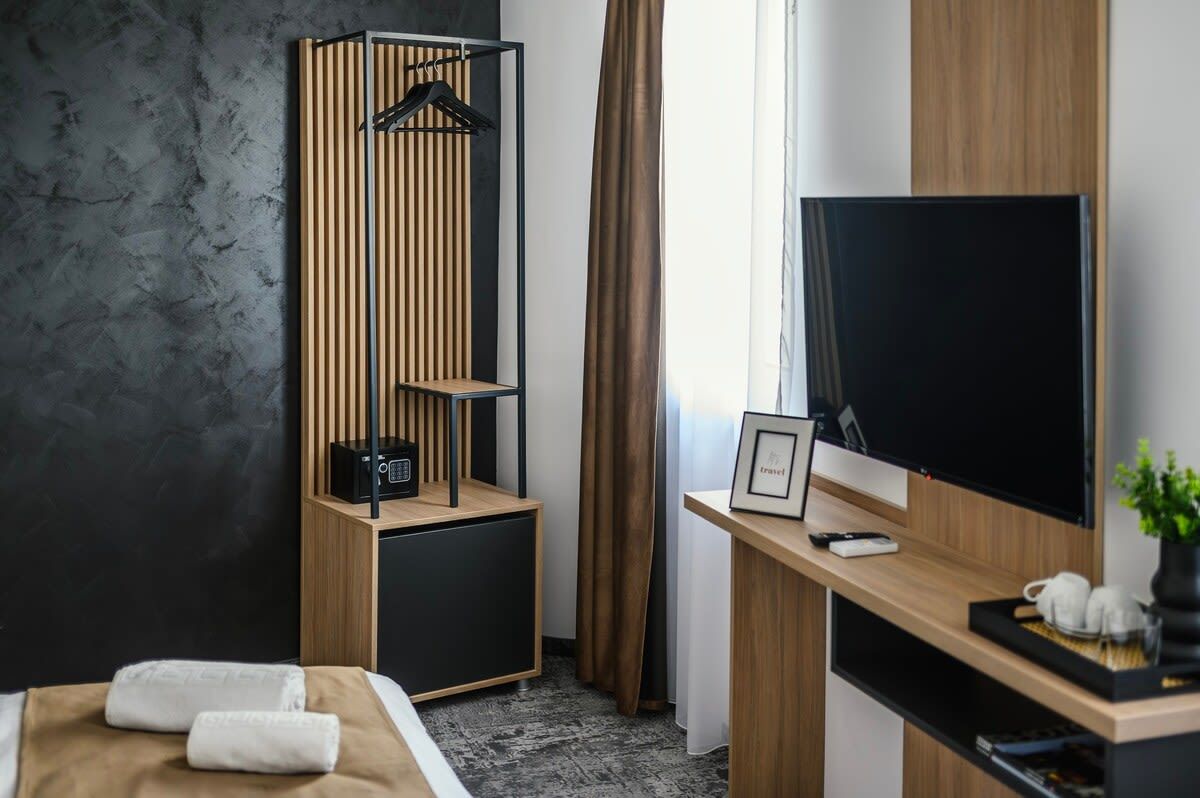 A hotel room with a bed, a TV, a desk with a computer, a coat rack, and a window with curtains.