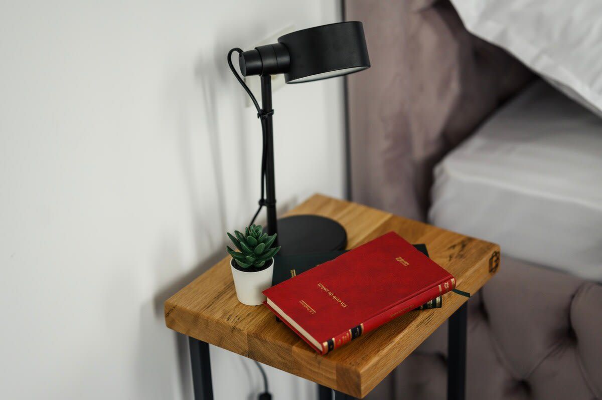 Een nachtkastje met een lamp, een kleine potplant en een rood boek.