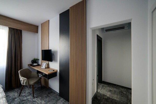 A modern hotel room with a desk, chair, TV, and a large wooden panel on the wall. - GBU Home - Olive Tween Room 206 (Timișoara)