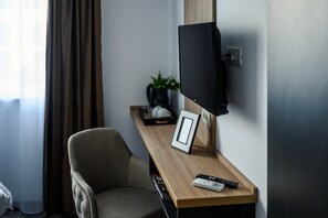 A hotel room with a wooden desk, a television mounted on the wall, a chair, a potted plant, and a framed picture. - GBU Home - Olive Tween Room 206 (Timișoara)