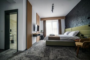 A modern hotel room with a large bed, a desk, a TV, and a view of the city. - GBU Home Timisoara - Olive 302 (Timișoara)