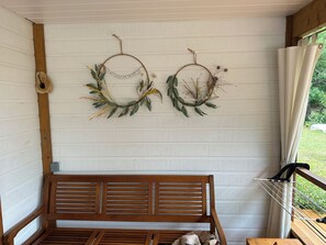 Relax on the porch with a comfortable bench and a small table, surrounded by natural elements and a drying rack.