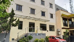 A hotel named "HOTEL METRO" with a modern facade, a staircase leading to the entrance, and several potted plants in front.