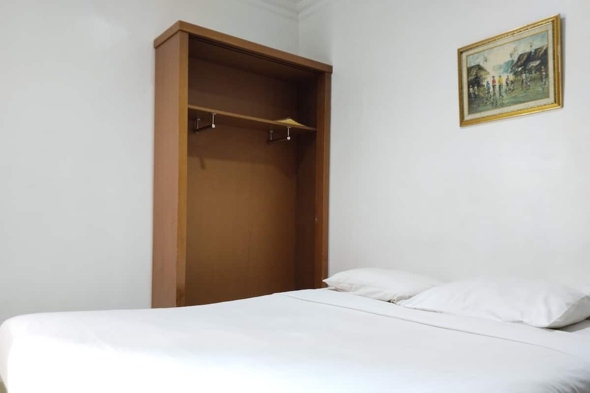 A bedroom with a bed, a wooden wardrobe, and a painting on the wall.