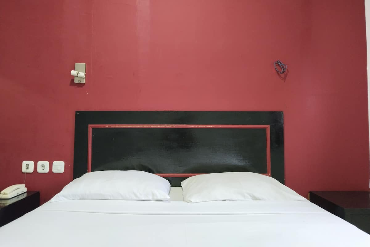 A hotel room with a red wall, a black headboard, white bedding, and a bedside telephone.