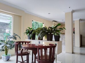 A dining area with a round wooden table and chairs, potted plants, and a view of greenery outside. - Metro Hotel Bekasi by Cocotel (Bekasi)