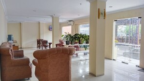 A spacious lobby with a high ceiling, a seating area with sofas and chairs, a dining table with chairs, and large windows offering a view of the street.