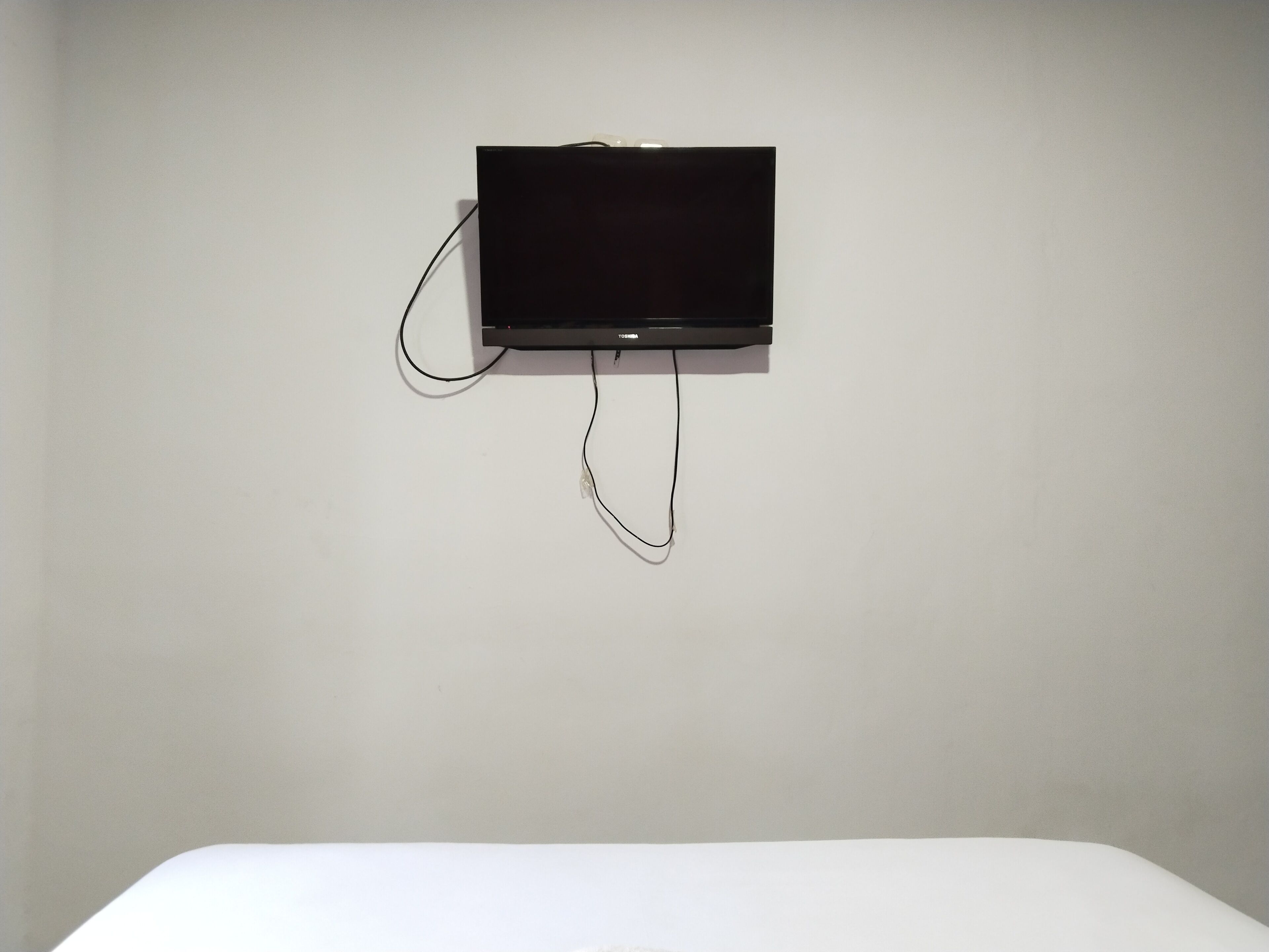 A black flat-screen TV mounted on a plain white wall with a cable connected to it.