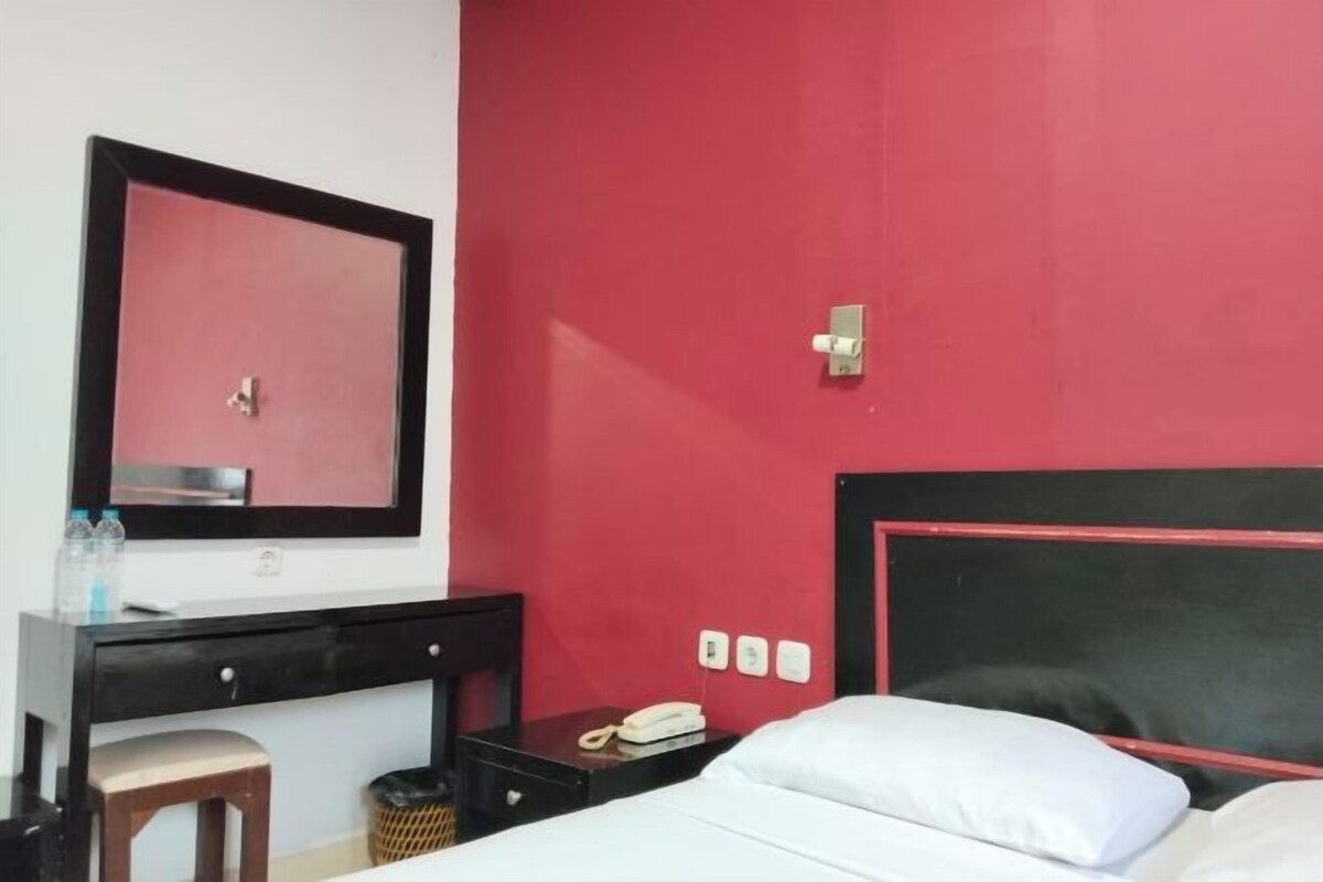 A hotel room with a bed, a desk with a chair, a mirror, and a telephone.