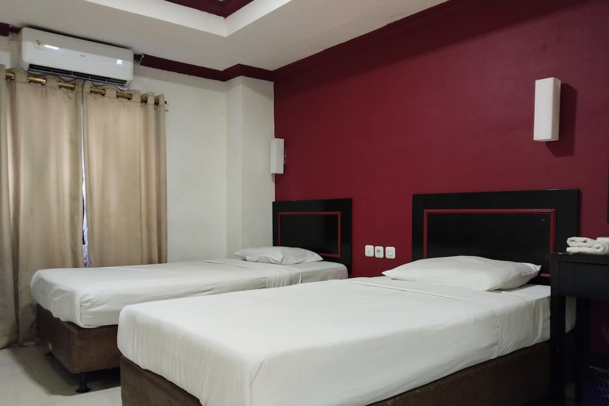 A hotel room with two single beds, a red accent wall, a ceiling fan, and an air conditioning unit.