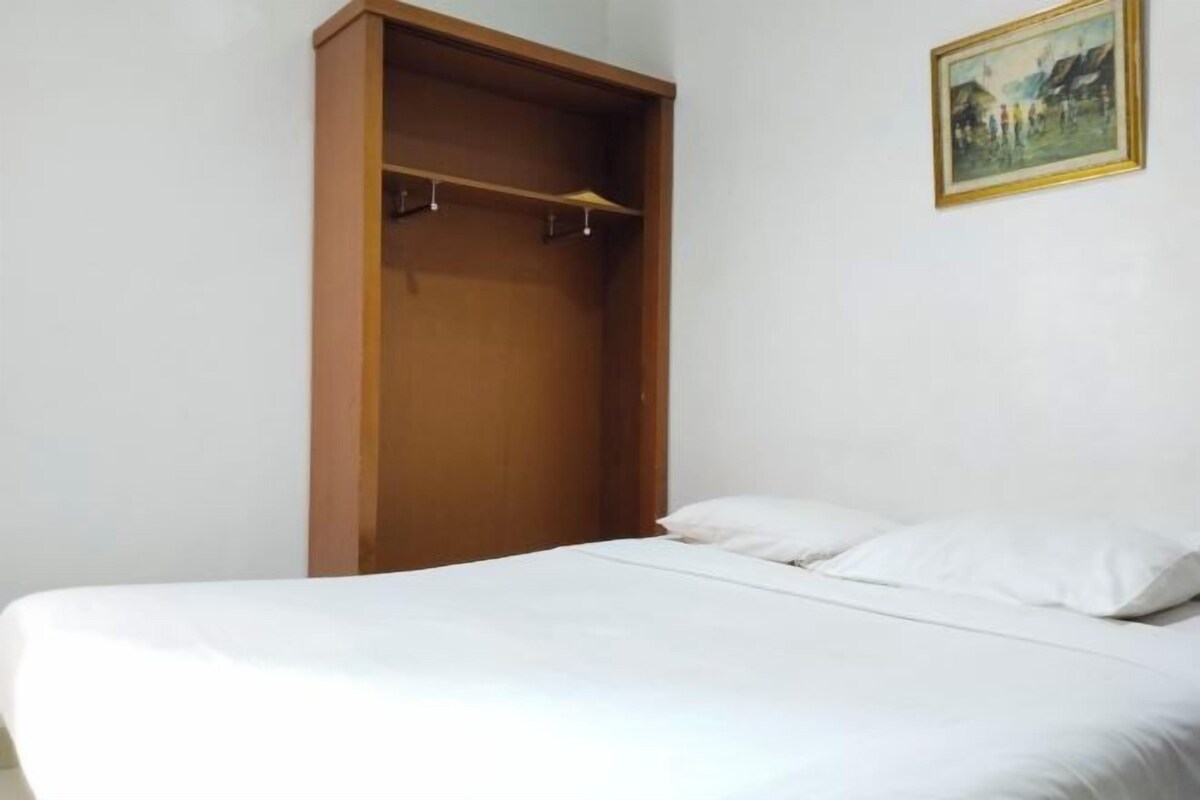 A bedroom with a bed, a wooden wardrobe, and a framed picture on the wall.