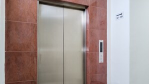 An elevator with a control panel and a trash bin beside it.