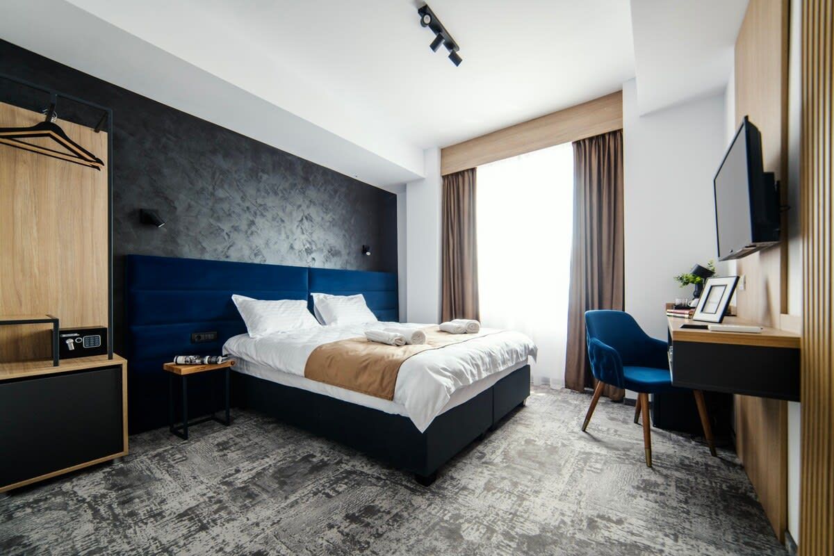 A modern hotel room with a large bed, a desk, a chair, and a wardrobe.
