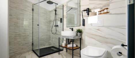 A modern bathroom with a glass-enclosed shower, a white toilet, and a marble-tiled floor.