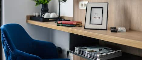A modern room with a blue chair, a wooden shelf with books, a framed picture, and a small plant.