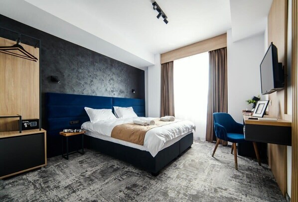Una habitación de hotel moderna con una cama grande, un escritorio, una silla y un armario.