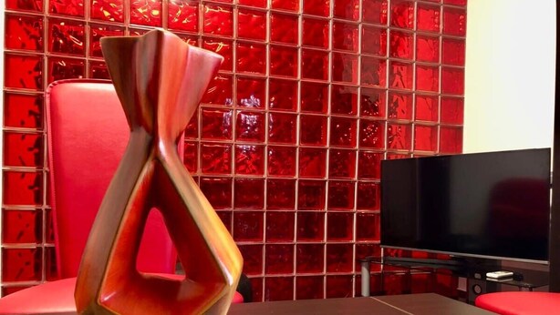 A modern interior with a red and black color scheme, featuring a unique abstract sculpture on a glass table, a red chair, and a flat-screen TV against a red tiled wall. - Joy City Stay Martirilor Giroc 4 (Timișoara)