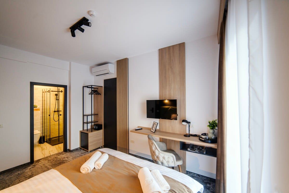 A modern hotel room with a bed, a desk, a chair, a TV, and a shower area.