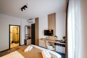 A hotel room with a bed, a desk, a chair, a TV, and a shower area. - GBU Home Olive Room 306 (Timișoara)