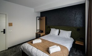 A hotel room with a bed, a bedside table, a wardrobe, and a coat rack.
