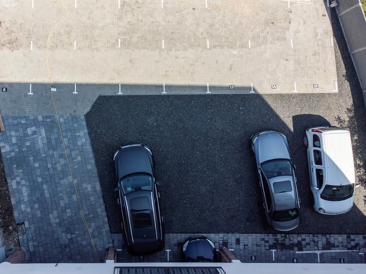 An aerial view of a parking lot with three cars and a white van.