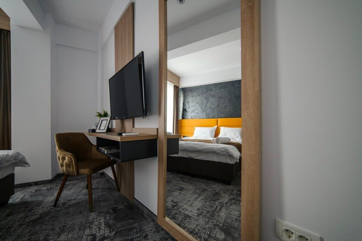 Una habitación de hotel con cama, escritorio con televisor, silla y un espejo grande.