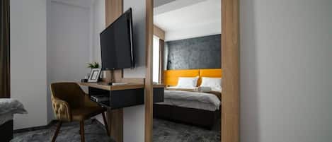 Una habitación de hotel con cama, escritorio con televisor, silla y un espejo grande.