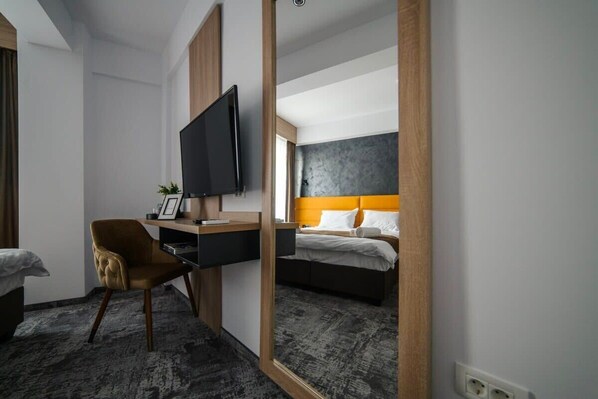 Une chambre d’hôtel avec un lit, un bureau avec une télévision, une chaise et un grand miroir.