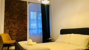 Un dormitorio con una cama grande, una silla, una mesita y una pared de ladrillo.
