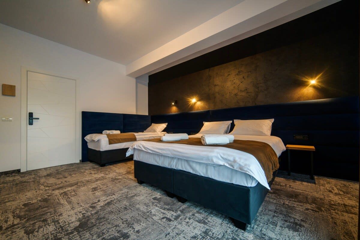 A modern hotel room with a large bed, dark headboard, and a textured floor.