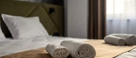 A neatly made bed with rolled white towels and a brown bedspread.