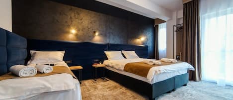 A hotel room with two beds, a large dark headboard, and a view of the outdoors.