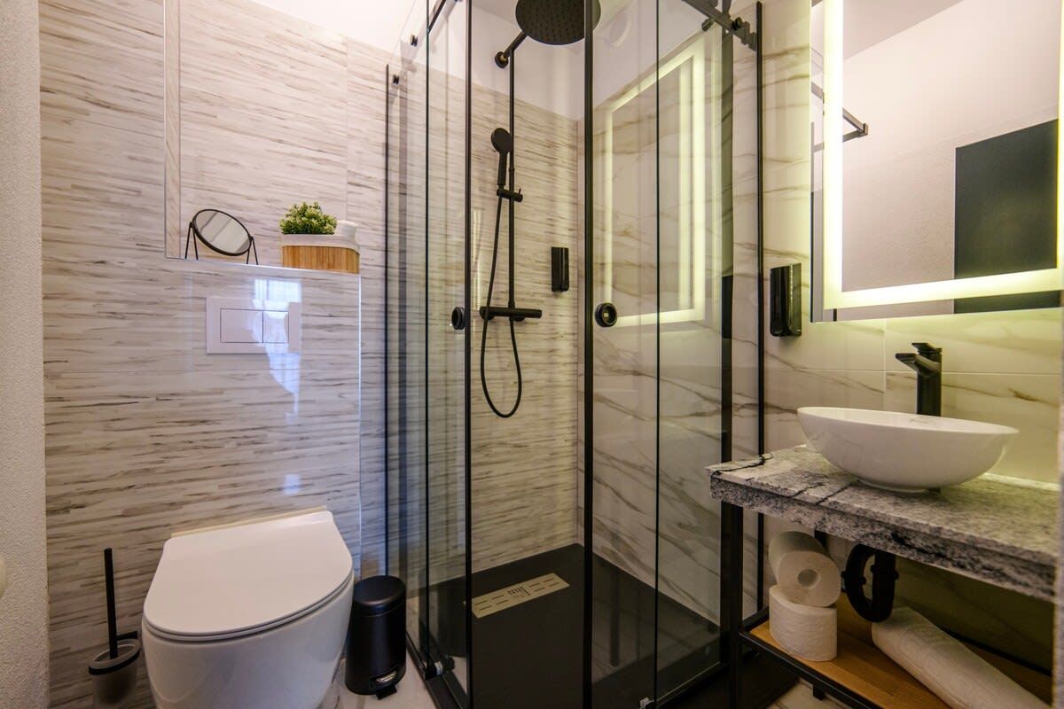 A modern bathroom with a glass-enclosed shower, a white toilet, a marble countertop, and a large mirror.