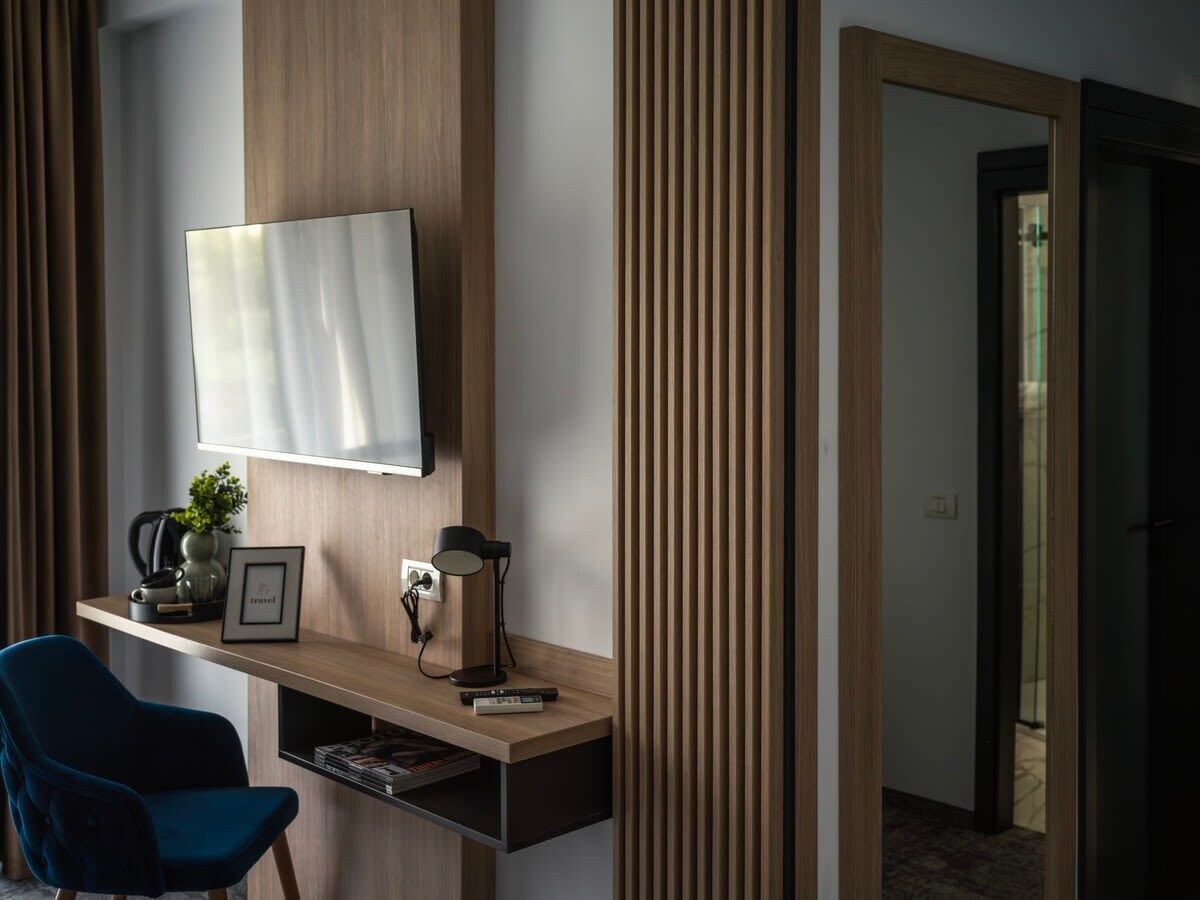 A modern hotel room with a wooden desk, a flat-screen TV, a blue chair, a coffee maker, and a framed picture.
