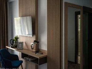 A modern hotel room with a wooden desk, a flat-screen TV, a blue chair, a coffee maker, and a framed picture. - GBU Home  Olive Executive 403 (Timișoara)